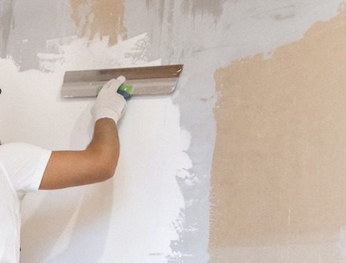 Male painter with a spatula in his hands makes repairs in home. Room renovation concept.